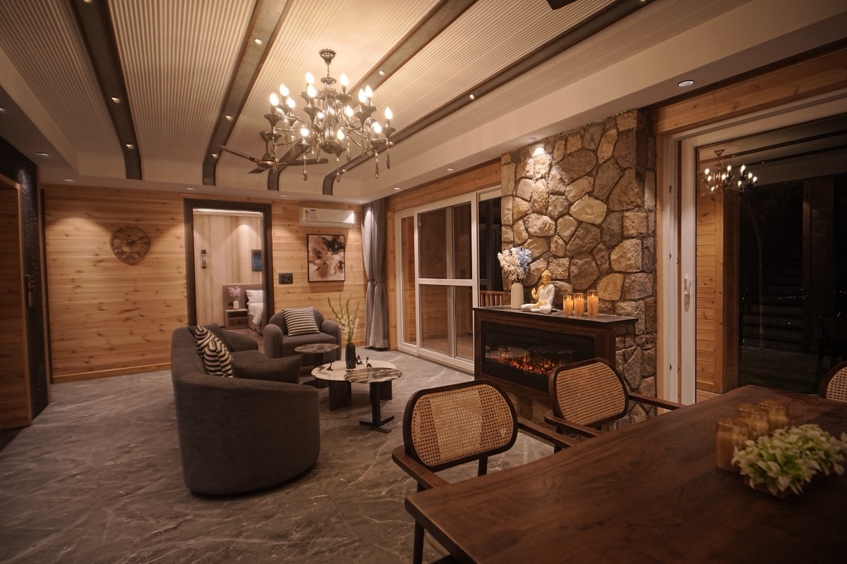 Luxury furnished living room with stone fireplace, cane chairs, and chandelier in Hillcrest Dehradun